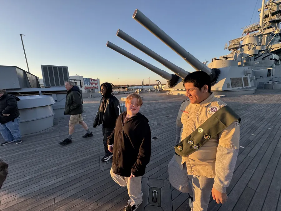 Scouts walking the teak deck of the USS Alabama beneath the raised barrels of a sixteen-inch main gun turret.