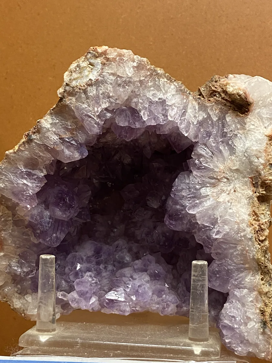 A large amethyst geode split open on a clear display stand, its hollow lined with pale purple crystals.