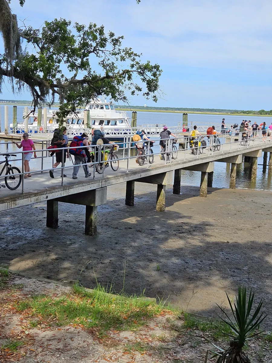 The ferry Cumberland Queen II tied up at a long concrete pier, with visitors crossing it carrying packs and pushing loaded bicycles.