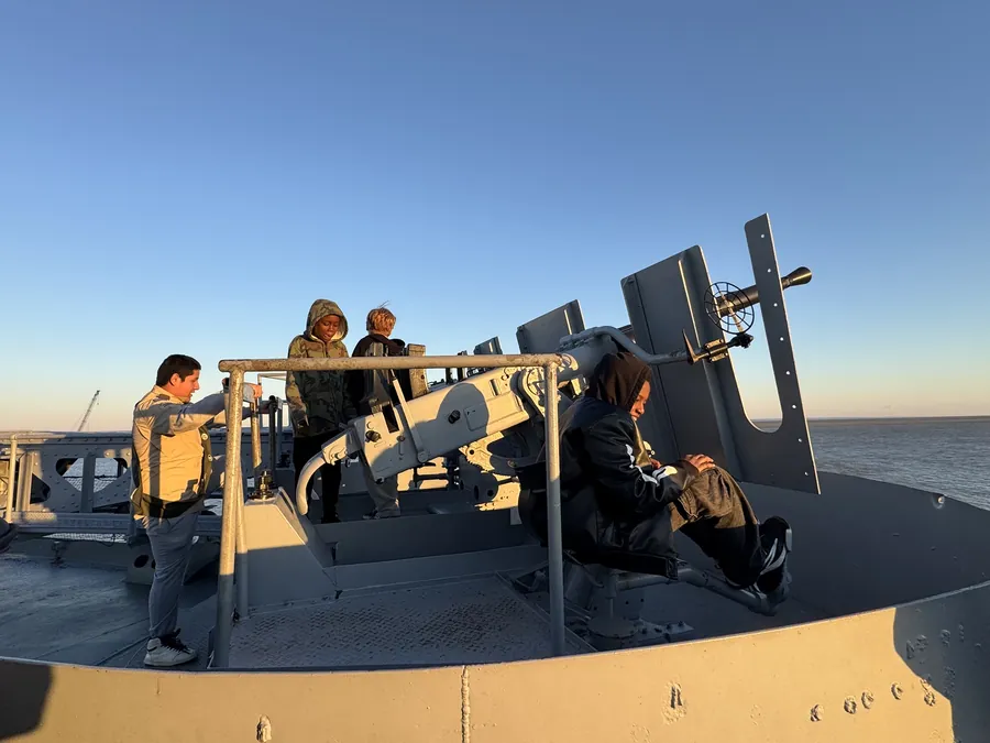 Scouts on the deck of the USS Alabama at sunset, silhouetted against the sky.